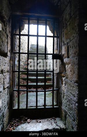 Ein mittelalterliches Kerker in Frankreich verfügt über dicke Steinmauern und ein Gitterfenster mit beleuchteten Steintreppen. Stockfoto