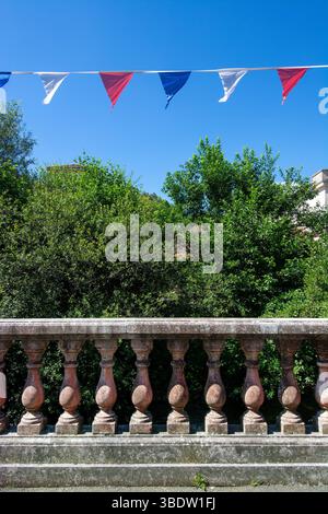 Eine dekorative Balustrade zeigt eine Reihe französischer Fahnen, die im Wind flattern, vor dem Hintergrund üppiger grüner Bäume und eines hellblauen Himmels Stockfoto