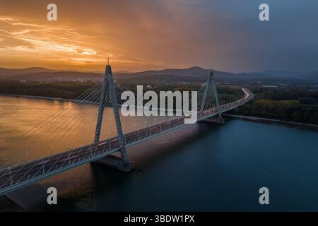 Budapest, Ungarn - aus der Vogelperspektive auf die Megyeri-Brücke über die Donau in der Abenddämmerung mit einem wunderschönen dramatischen goldenen Sonnenuntergang und den Buda-Hügeln Stockfoto