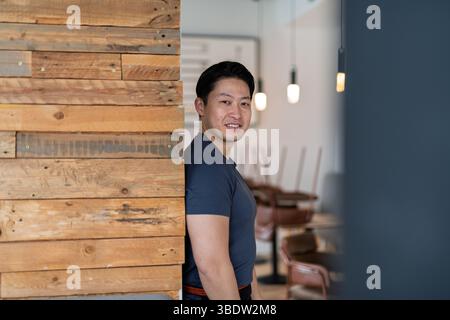 Athletischer asiatischer Mann, der in die Kamera schaut, als Kellner arbeitet. Stockfoto