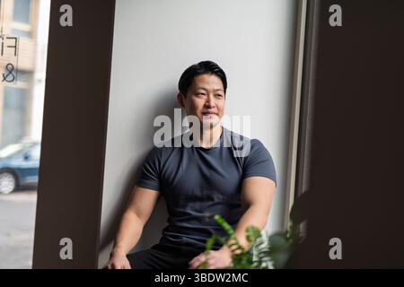 Selbstbewusster junger Mann, der bei Tageslicht am Fenster sitzt Stockfoto