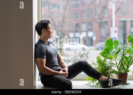 Selbstbewusster junger Mann, der bei Tageslicht am Fenster sitzt Stockfoto