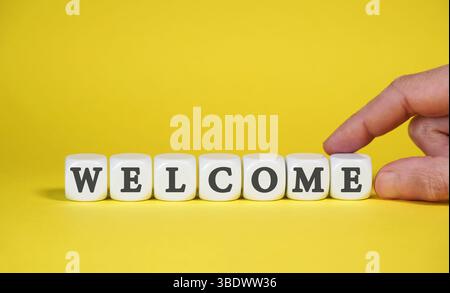 Begrüßungsschild mit Wort und Schrift auf weißen Würfeln auf gelbem Hintergrund für Begrüßungskonzept. Stockfoto