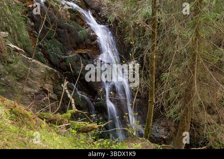 Eine wunderschöne Langzeitaufnahme eines Wasserfalls, der über moosige Felsen in einem Wald stürzt, mit einer friedlichen Atmosphäre. Stockfoto