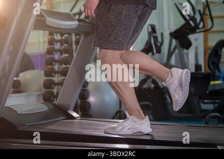 Ein Mann läuft auf einem Laufband in einem Fitnessstudio. Der Mann trägt Shorts und ein weißes Hemd Stockfoto