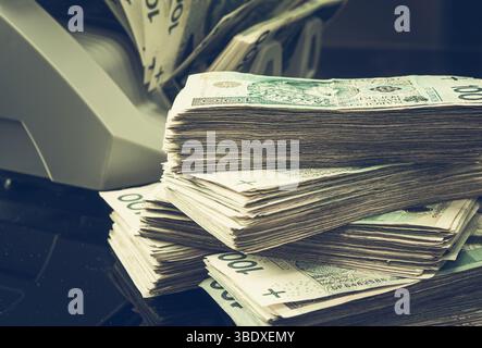 In einem Geschäftsumfeld werden polnische Zloty-Banknoten ordentlich neben einem Geldzählautomaten gestapelt. Stockfoto