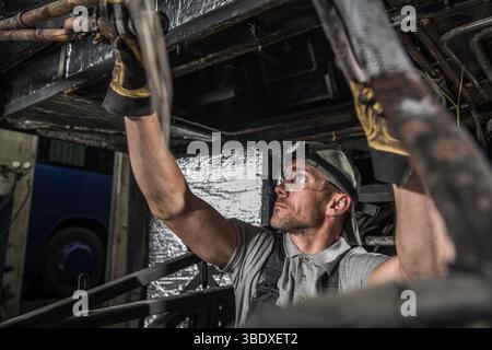 Ein Mechaniker inspiziert die Unterseite eines Fahrzeugs in einer Werkstatt, stellt die Werkzeuge ein und konzentriert sich auf die anstehende Aufgabe. Stockfoto