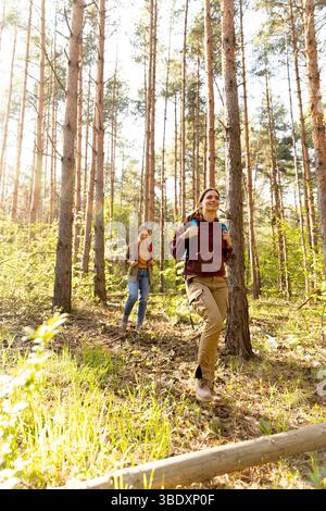Freunde erkunden gerne einen ruhigen Kiefernwald, während das Sonnenlicht durch hohe Bäume strömt und eine lebendige Atmosphäre voller Abenteuer und Kameradschaft schafft. Stockfoto