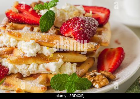 Belgische oder Wiener Waffeln mit Frischkäse, Erdbeeren und Nüssen auf einem weißen Teller mit Minzzweigen. Nahaufnahme. Hochwertige Fotos Stockfoto