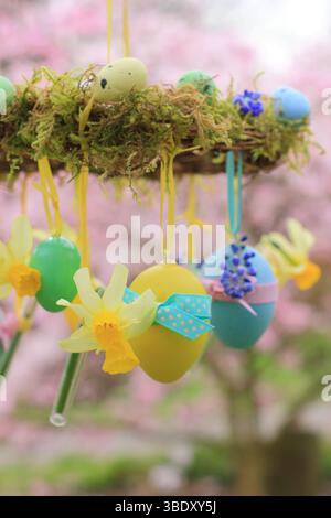 Osterkranz. Einfach zu badizierendes Kranzprojekt mit Moos, Miniatur-Narzissen und Osterei, aufgehängt auf Gartenzweig mit gelbem Band. UK Stockfoto
