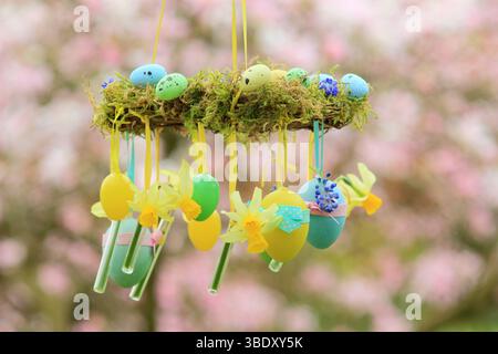 Osterkranz. Einfach zu badizierendes Kranzprojekt mit Moos, Miniatur-Narzissen und Osterei, aufgehängt auf Gartenzweig mit gelbem Band. UK Stockfoto