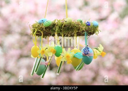 Osterkranz. Einfach zu badizierendes Kranzprojekt mit Moos, Miniatur-Narzissen und Osterei, aufgehängt auf Gartenzweig mit gelbem Band. UK Stockfoto