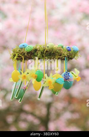 Osterkranz. Einfach zu badizierendes Kranzprojekt mit Moos, Miniatur-Narzissen und Osterei, aufgehängt auf Gartenzweig mit gelbem Band. UK Stockfoto