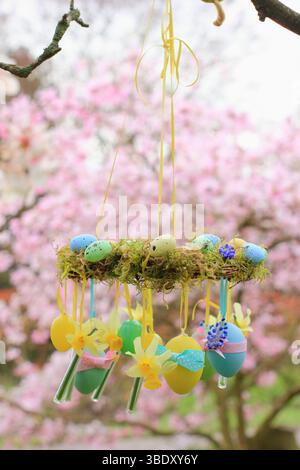 Osterkranz. Einfach zu badizierendes Kranzprojekt mit Moos, Miniatur-Narzissen und Osterei, aufgehängt auf Gartenzweig mit gelbem Band. UK Stockfoto