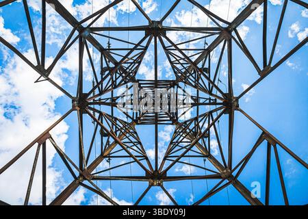 Abstraktes geometrisches Muster eines elektrischen Pylons von unten vor einem hellblauen Himmel, ideal für industrielle oder abstrakte Hintergründe Stockfoto