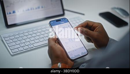 Finanzanalyst überprüft Echtzeitaktien, Börsenmarktdiagramme auf Smartphone und digitalem Tablet mit der Online Trading App. Afroamerikanischer Geschäftsmann, der im Investment Bank Office arbeitet. Nahaufnahme. Stockfoto