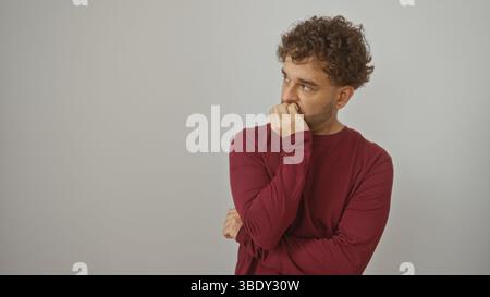 Nachdenklicher junger Mann mit lockigen Haaren, der roten Pullover auf weißem Hintergrund trägt Stockfoto