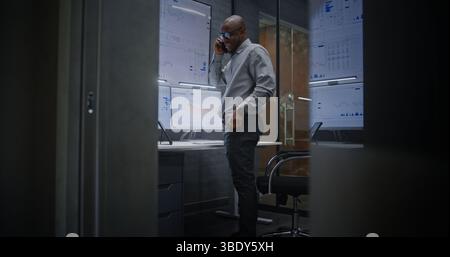 Advanced Trading Office: Begeisterte Finanzanalysten telefonieren, nachdem sie rentable Investitionen getätigt haben. Afroamerikanischer Geschäftsmann freut sich über einen erfolgreichen Finanzvertrag oder Vertrag. Stockfoto