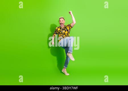 Ein glücklicher Mann mittleren Alters in einem lebhaften Sommershirt posiert energisch vor einem hellgrünen Hintergrund und strahlt Spaß und Charisma aus Stockfoto