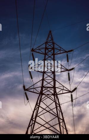 Ein hoher Hochspannungsturm aus Stahl steht vor einem blauen Himmel mit verstreuten Wolken. Das Bild erfasst die Infrastruktur der Stromversorgung Stockfoto