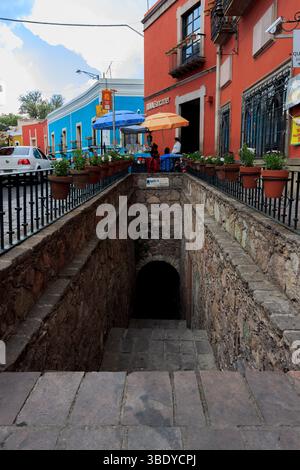 Guanajuato City, Mexiko - 30. Mai 2016: Menschen sitzen an einem Stand in der Nähe eines BBVA Bancomers, oberhalb eines Steintunneleingangs an einem sonnigen Tag. Stockfoto