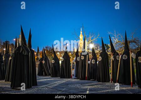 Nazarener aus der Hermandad de Santa Genoveva treffen sich zu einer feierlichen Prozession in Sevilla, Andalusien, um die Karwoche in der Abenddämmerung zu feiern. Stockfoto