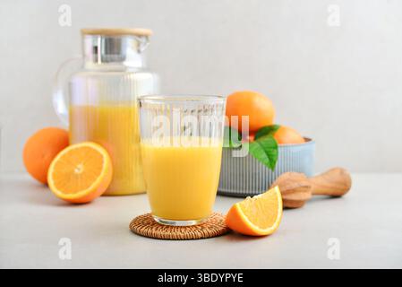 Orange frisch gepresster Saft in Glas und Gläsern Kanne mit Reifen Orangen und Olivenholz Presse auf hellem Hintergrund Stockfoto
