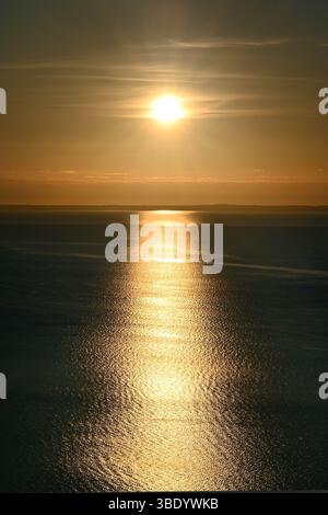 Sonnenreflexionen auf der ruhigen Wasseroberfläche mit subtilen Wellen beim Sonnenaufgang am Balaton im vertikalen Format Stockfoto