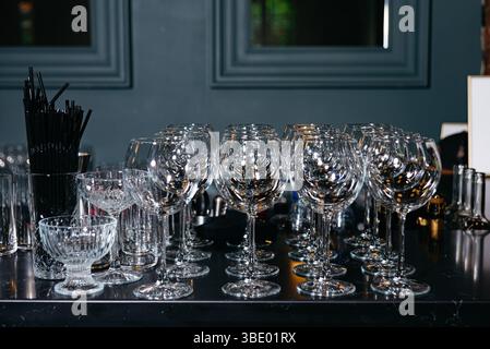 Ordentlich gestapelte saubere Weingläser und anderes Trinkgeschirr auf einer schwarzen Bartheke, bereit für eine Veranstaltung oder ein Restaurant. Stockfoto