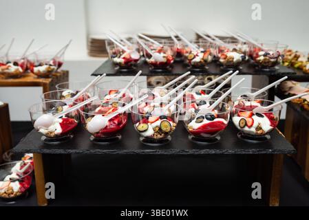 Eine Präsentation klarer Tassen gefüllt mit Joghurt, Müsli und frischen Beeren, die ordentlich auf einem Catering-Buffet-Tisch serviert werden. Stockfoto