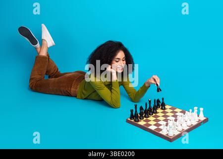 Junge Frau, die auf blauem Hintergrund Schach spielt, lächelt und genießt Freizeit, zeigt Fokus und Strategie Stockfoto