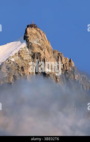 Gipfel der Aiguille du Midi mit alpinen Gebäuden, die aus dem Nebel vor klarem blauem Himmel ragen, im Sommer über Chamonix, Mont Blanc Massiv, Alpen Stockfoto