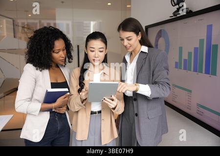 Multiethnische Berufsfrauen, die digitale Inhalte auf einem Tablet überprüfen oder diskutieren Stockfoto