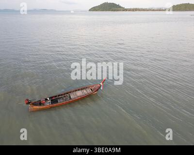 Drohnenaufnahme des Bootes, das an einer friedlichen Küste im blauen Wasser Thailands ankert, zeigt Motorboote und Segelboote, die in der Nähe eines Sandufers angedockt sind, umgeben von üppigen Palmen und einem wunderschönen Sommerhimmel. Stockfoto