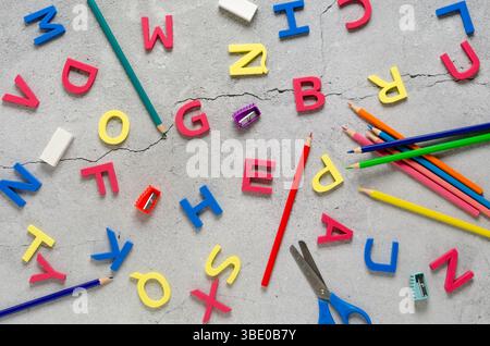Bunte Alphabetbuchstaben und Schulutensilien auf einer Betonoberfläche. Back-to-School-Konzept. Stockfoto