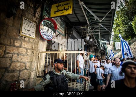 Jerusalem, Israel. 26. Mai 2025. Ein israelischer Grenzpolizist steht neben einem muslimischen Heim, während israelische rechte Jugendliche tanzen und ihre Nationalflagge schwenken, die am Montag, den 26. Mai 2025, durch das muslimische Viertel der alten Stadtmauer von JerusalemÕs marschieren. Zehntausende junger religiös-zionistischer und rechter Männer und Frauen marschierten durch die Hauptstadt und schwenkten Davidssterne Flaggen, die durch das muslimische Viertel in die Altstadt von Jerusalem eindrangen, als Teil eines umstrittenen flaggenmarsches, der die Wiedervereinigung der Stadt während des Sechstagekrieges IsraelÕs und die Eroberung des Tempelbergs und des Westens kennzeichnete Stockfoto