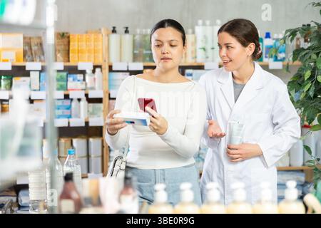 Frau, die Salbe scannt, während der Apotheker freundliche Unterstützung anbietet Stockfoto