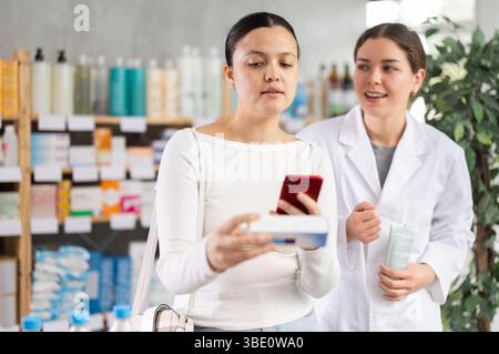 Frau, die Salbe scannt, während der Apotheker freundliche Unterstützung anbietet Stockfoto