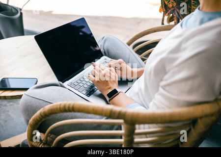 Nahaufnahme einer Frauenhände, die auf einem Laptop tippen, während sie in einem gemütlichen Café sitzen. Stockfoto