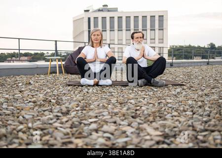 Älteres Paar, das zusammen Yoga auf einem urbanen Dach praktiziert Stockfoto
