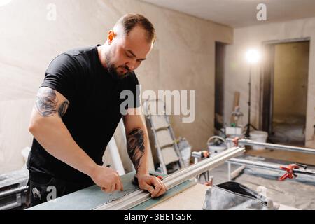 Builder preparing aluminum profiles for stretch ceiling using special equipment in apartment being renovated Stockfoto