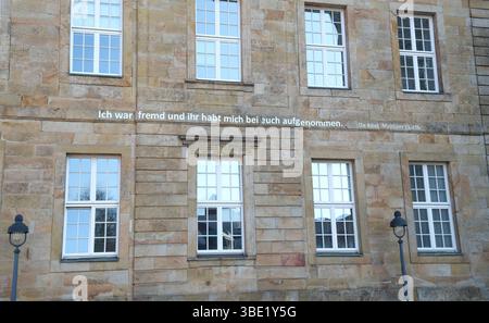 Steinfassade mit symmetrischen, weiß gerahmten Fenstern mit mehreren Scheiben. Ein Satz aus der Bibel auf Deutsch ist über das W eingeschrieben Stockfoto