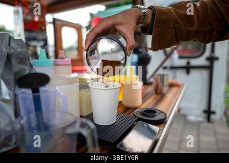 Männlicher Barista serviert Kaffee an einem Tisch. Ein kleines Unternehmen in einem Café oder Café auf einem Lkw Stockfoto