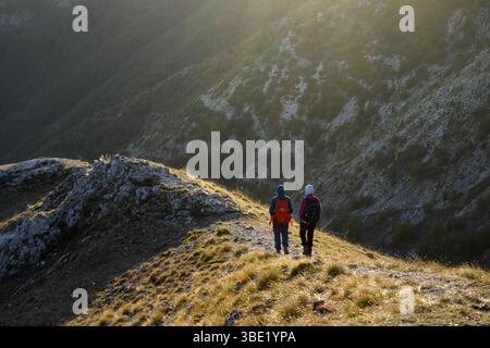 Rückansicht zwei Wanderer, die einen Bergrücken in einem Bergtal bei Sonnenuntergang hinuntergehen, Lukomir, Bosnien und Herzegowina Stockfoto