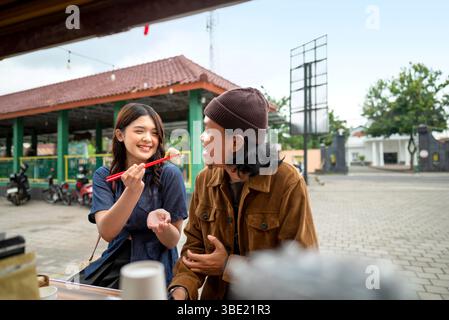 Indonesisches südostasiatisches Paar genießt Essen vor dem Laden. Ein kleines Unternehmen auf einem Lkw Stockfoto