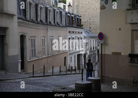 Einsame Figur auf der schrägen Kopfsteinpflasterstraße mit Pariser Mansardendächern und Fensterläden Stockfoto