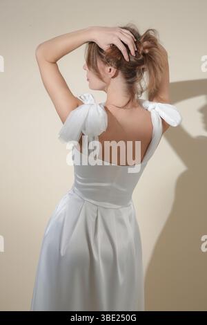 Serie von Studiofotos eines weiblichen Models in elegantem weißem Midikleid mit Schleifen an den Schultergurten Stockfoto
