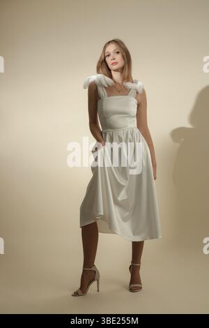 Serie von Studiofotos eines weiblichen Models in elegantem weißem Midikleid mit Schleifen an den Schultergurten Stockfoto