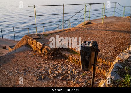 Mülleimer voller Glasflaschen morgens nach Partyabend am Strand an der Strandpromenade. Massentourismusproblem, Umweltverschmutzung Stockfoto