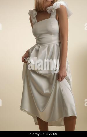 Serie von Studiofotos eines weiblichen Models in elegantem weißem Midikleid mit Schleifen an den Schultergurten Stockfoto